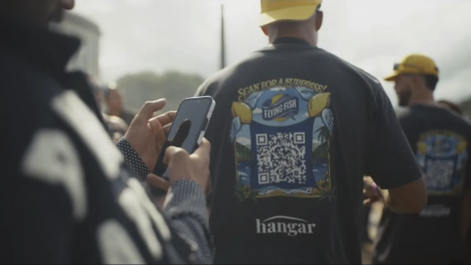 A phone scanning the QR code printed on a promoter's shirt at Hangar